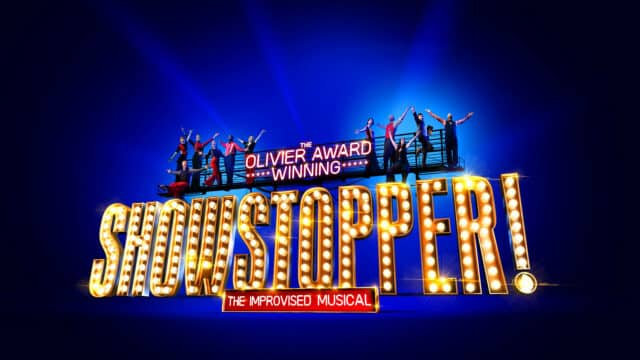 SHOWSTOPPER: The Improved Musical promotional image. A blue background with the words 'Showstopper!' made up of theatre lights. The actors in the show, wearing black and red clothing, stand on top of the letters with their arms raised above their heads.