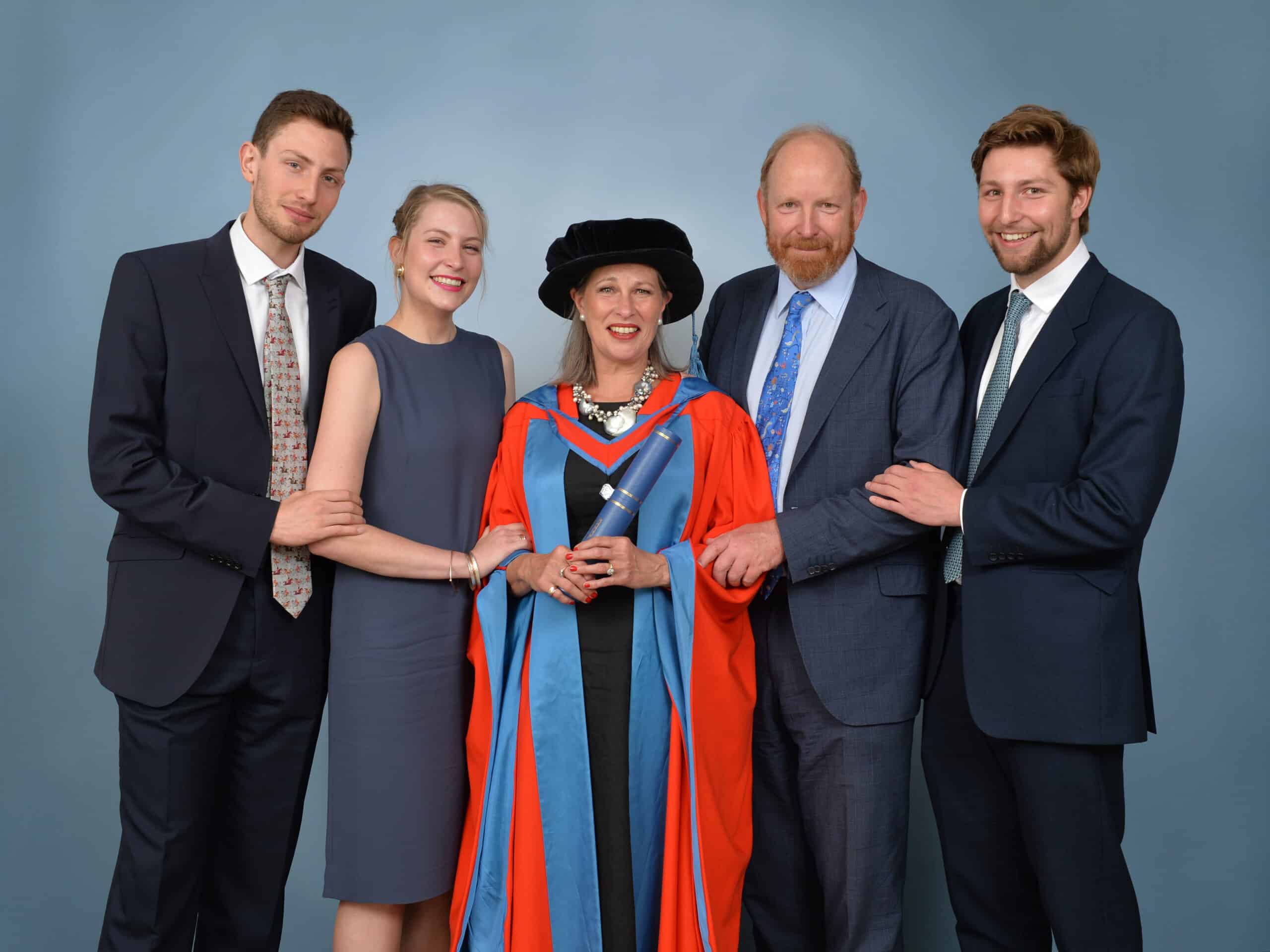 Photo of Lucy Studholme dressed in a graduation gown and hat, holding a diploma, with four family members