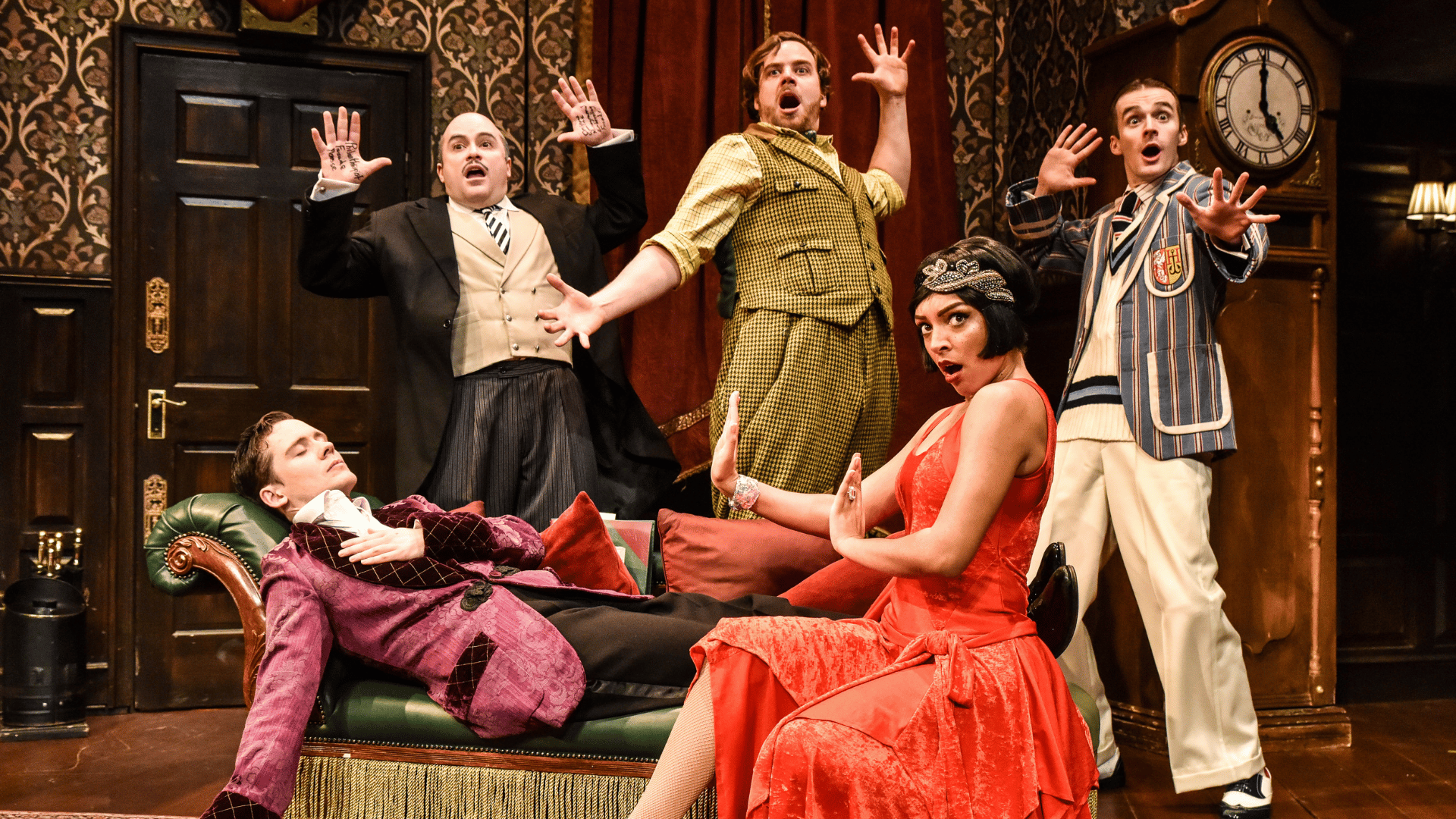 The Play That Goes Wrong Production Shot: Jonathan (Seán Carey) is laid down on a chaise longue with his eyes closed. He is surrounded by Dennis (Edward Howells), Robert (Matthew Howell), Sandra (Laura White) and Max (Tom Babbage) who all are looking towards the audience with shocked looks on their faces.