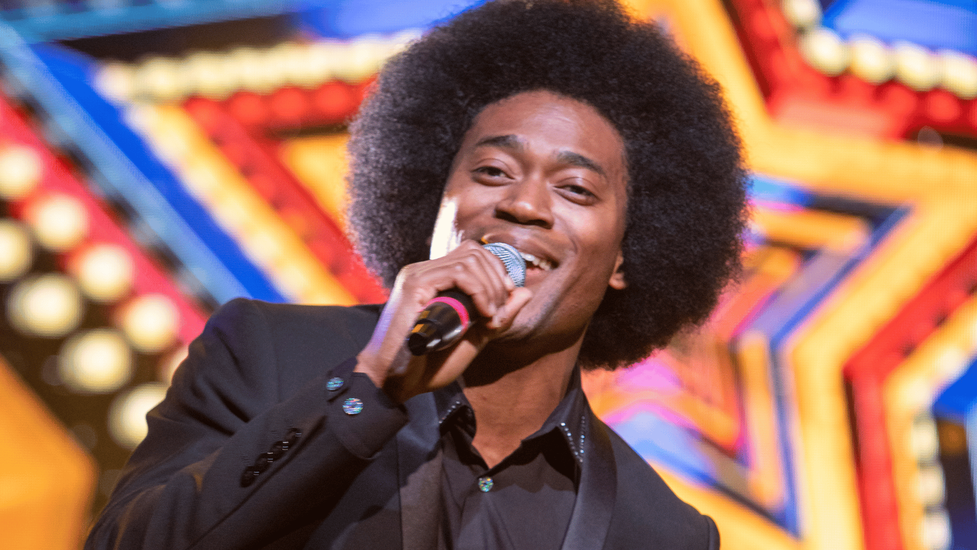 Lost in Music production shot: a close up of one of the male singers, who has a large afro and wear a smart suit
