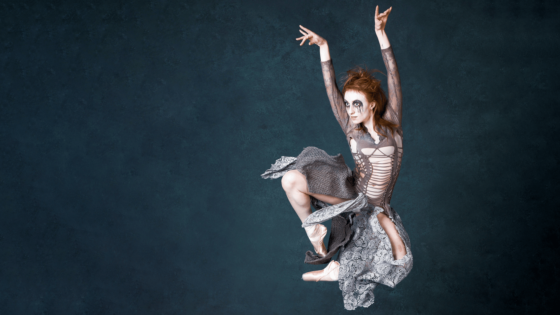 A ballet dancer with red hair leaps off the ground