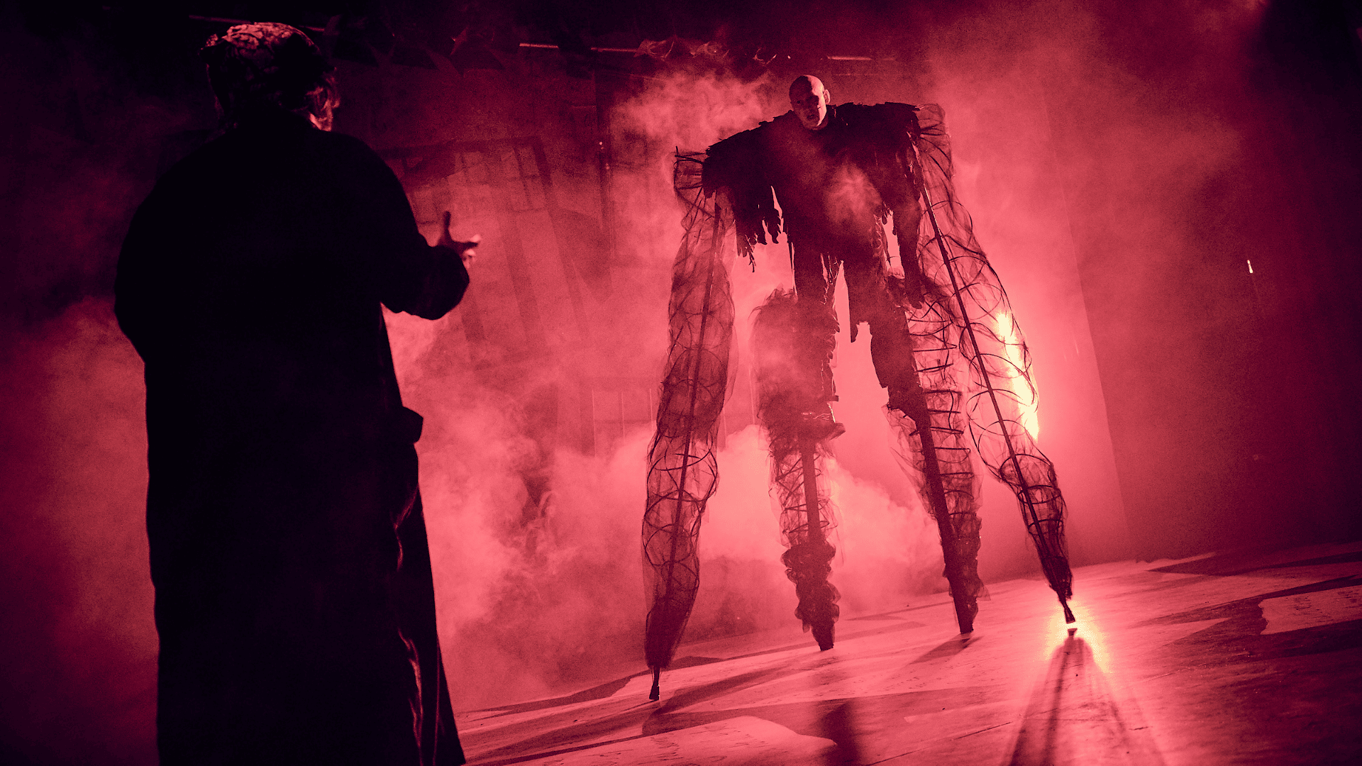 Christmas Carol production shot: An actor on stilts creates a look of a large ghostly monster. Smoke and red lighting fills the image