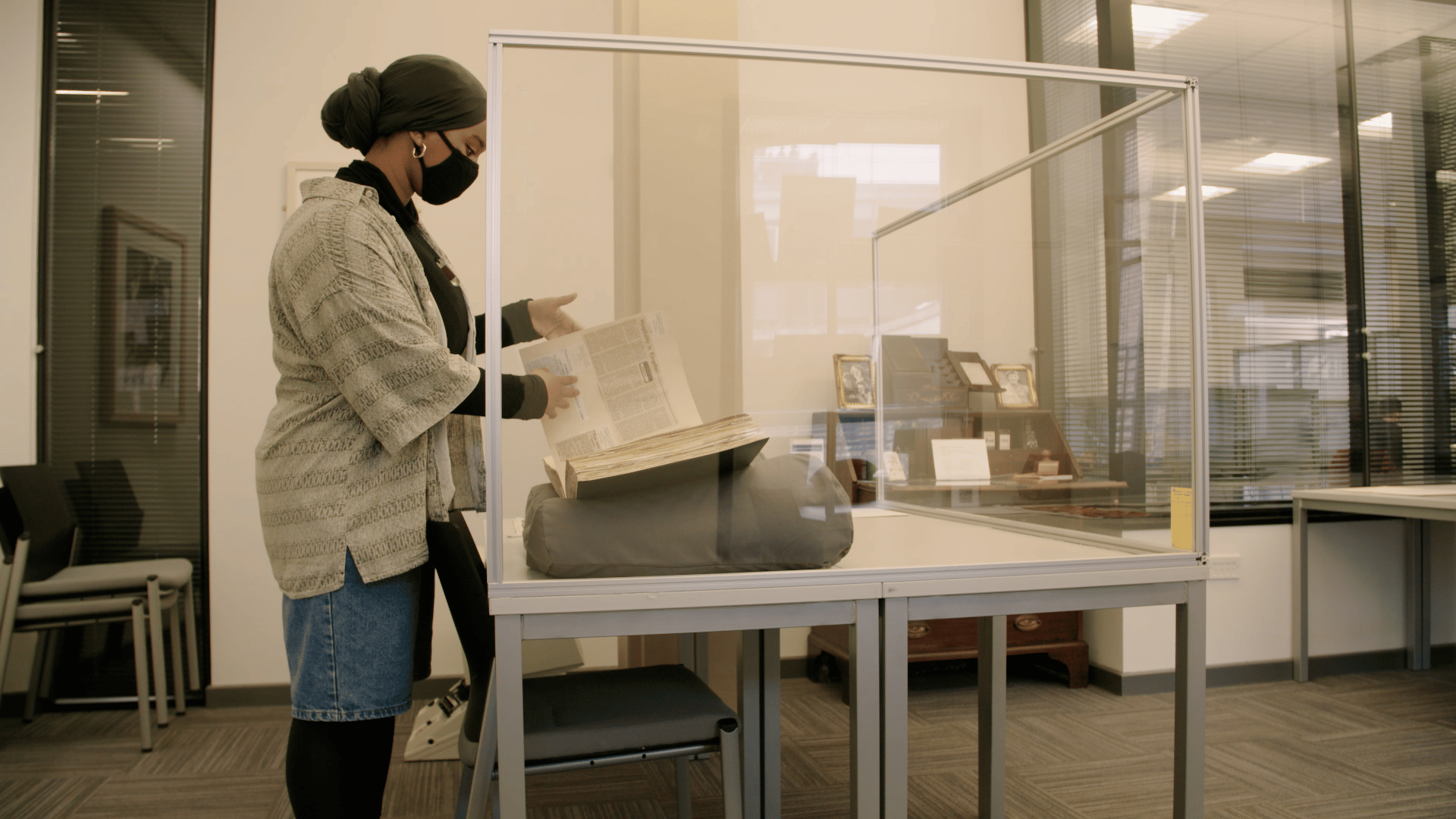 A female intern dressed in a lab coat and gloves inspects a book in the archive