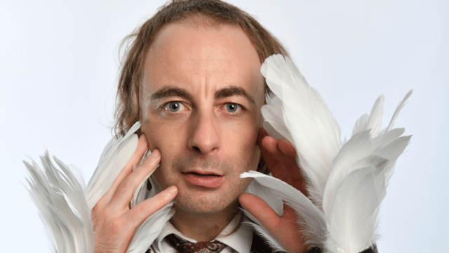 PAUL FOOT: SWAN POWER artwork. Paul Foot looking straight ahead, wearing a shirt and tie with a black leather jacket, he holds his hands up to his face with swan feathers emerging from his sleeves.