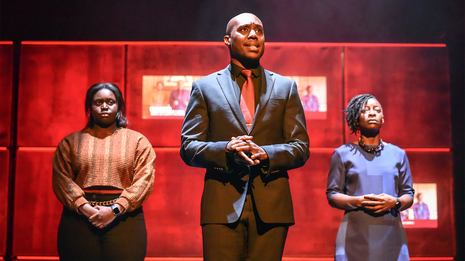 Noughts and Crosses production photo: (L-R) Steph Asamoah (Minerva), Chris Jack (Kamal) and Amie Buhari (Jasmine) stand together in a line. They are each clasping their hands.