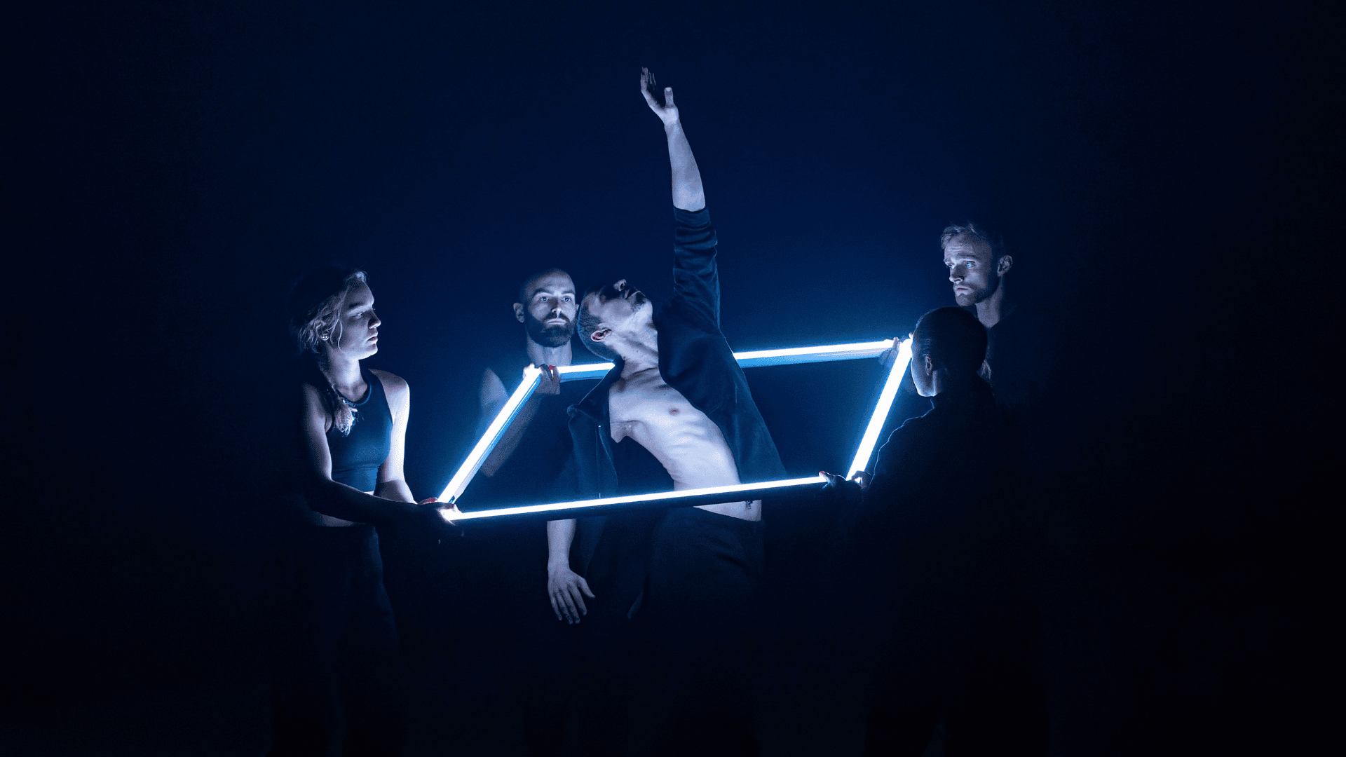 Lewis Major's Satori: A male dancer with open shirt is reaching up through a 3D light box, held up by other dancers