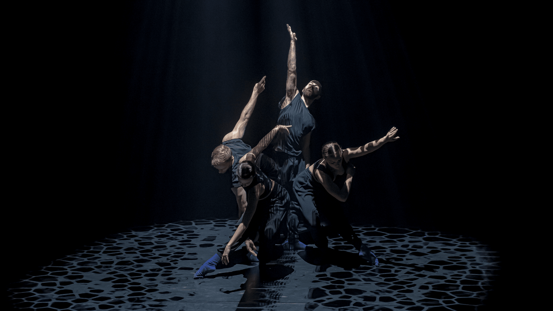 Lewis Major's Unfolding: Two male and two female dancers are creating a triangular form; one central reaching up to the sky, the others around him crouched and bending forward, their arms reaching up behind them and to the side