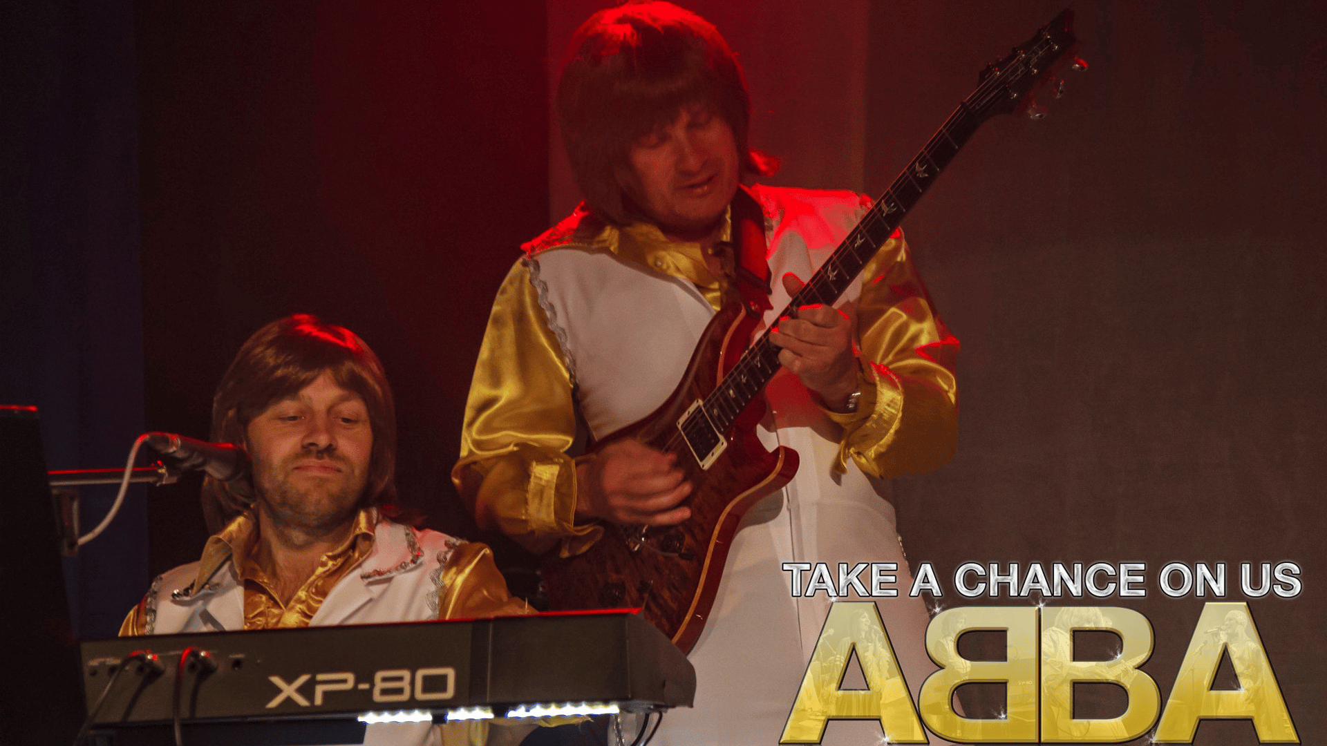 The Benny and Bjorn tribute performers next to each other in white and gold all-in-one outfits, playing guitar and keys.