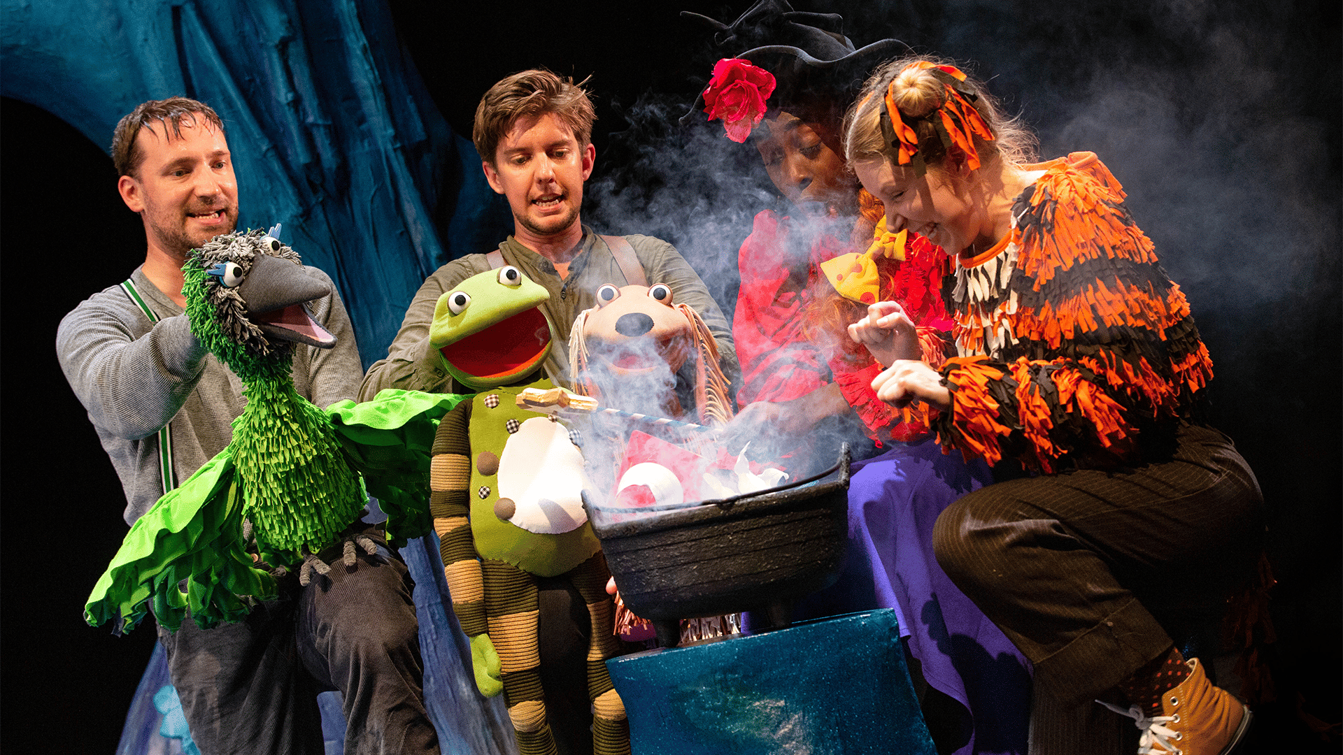 The witch, bird, frog, dog, cat and cast members gather around a smoking cauldron.