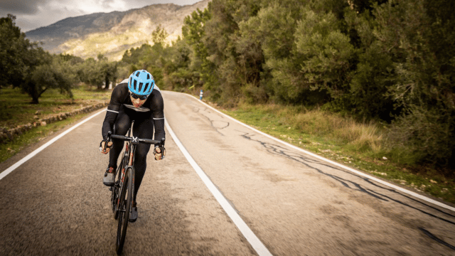 A picture of Mark Beaumont riding a bicycle down a scenic road with mountains in the background.