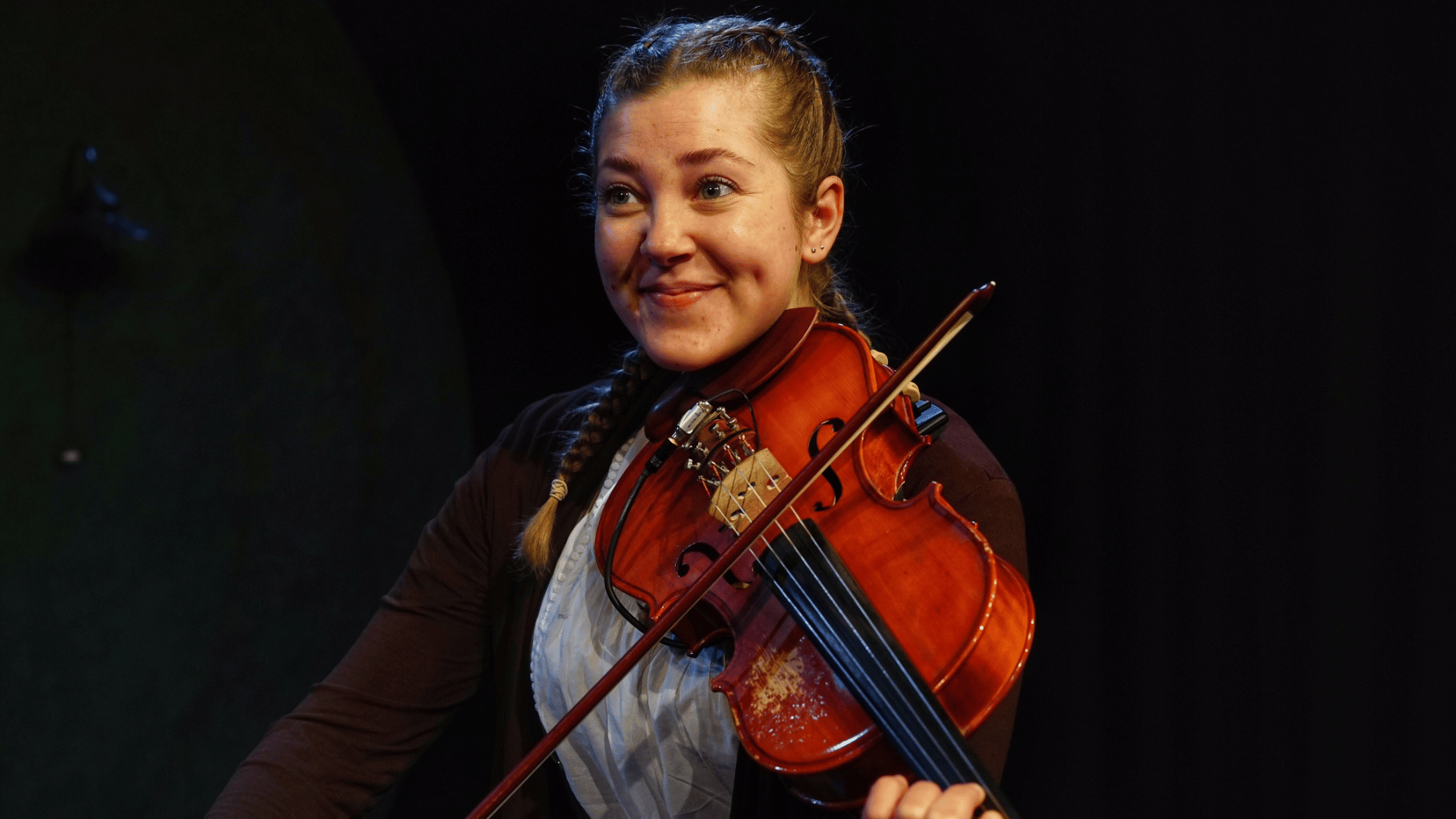 A woman smiling while playing a violin.