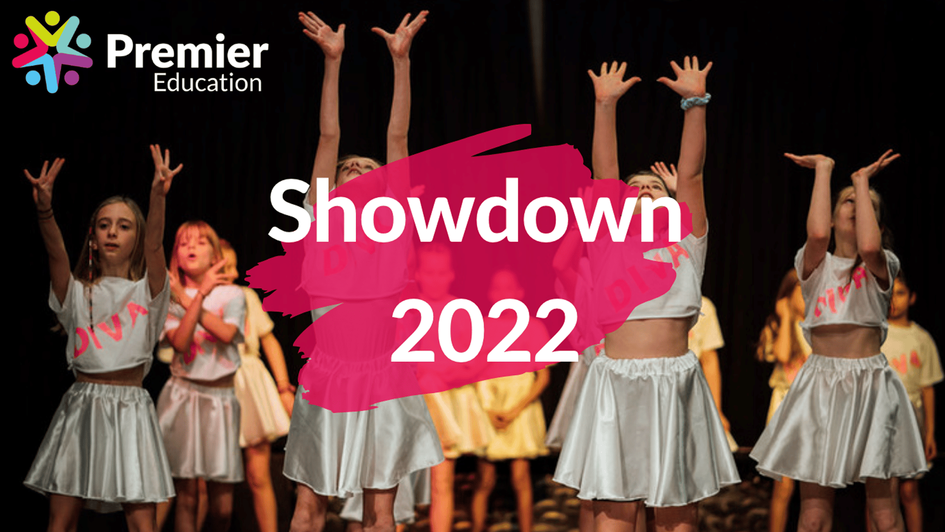 Children wearing white tops and white skirts holding their arms in the air as part of a dance routine. The picture is overlayed with a pink splodge with the words 'Showdown 2022' written over the top. The Premier Education logo is in the top left corner.