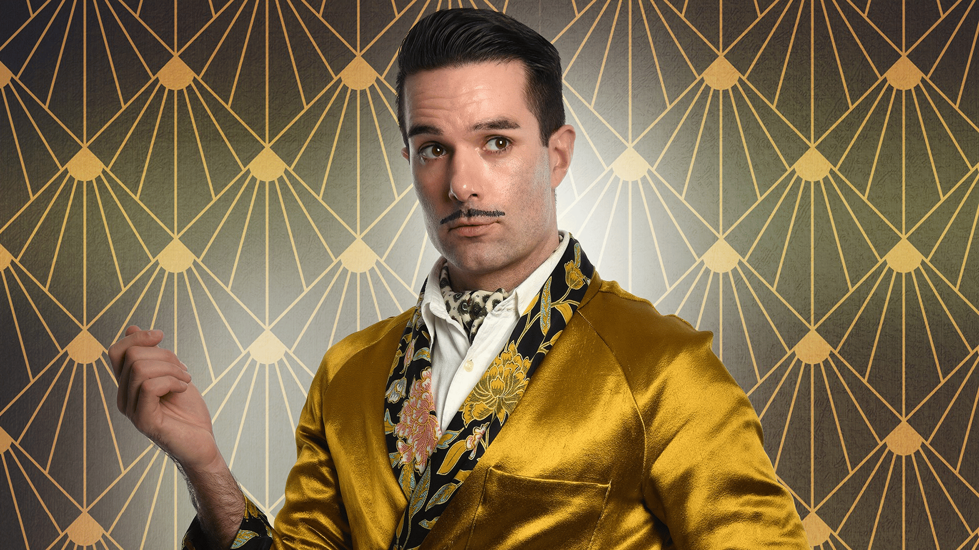 Troy Hawke wearing a golden silk dressing gown, holding his right arm up at shoulder height and looking off towards the left. His dark hair is very neat and he has a pencil moustache. The background is a black and gold 20's style wallpaper.