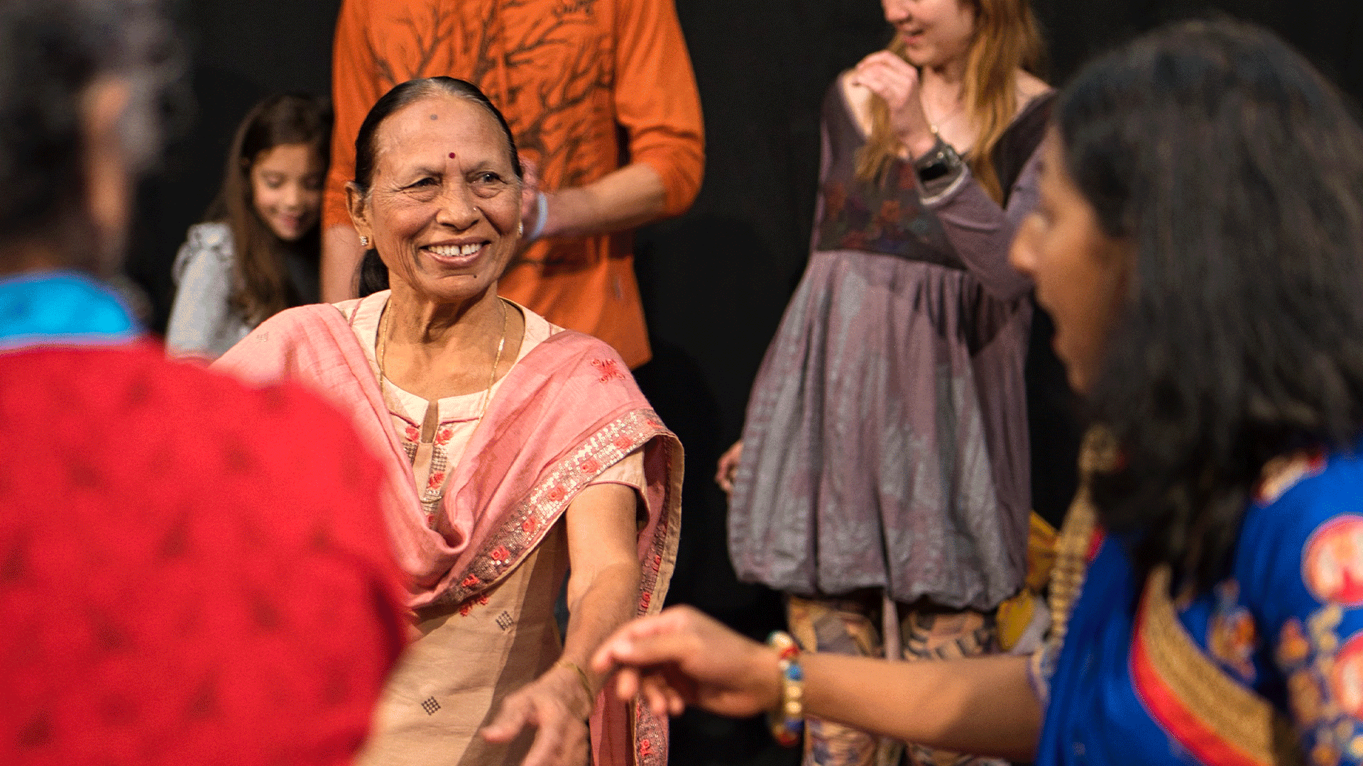 A smiling woman wearing traditional Garba dance dress reaches out to another women mid-dance