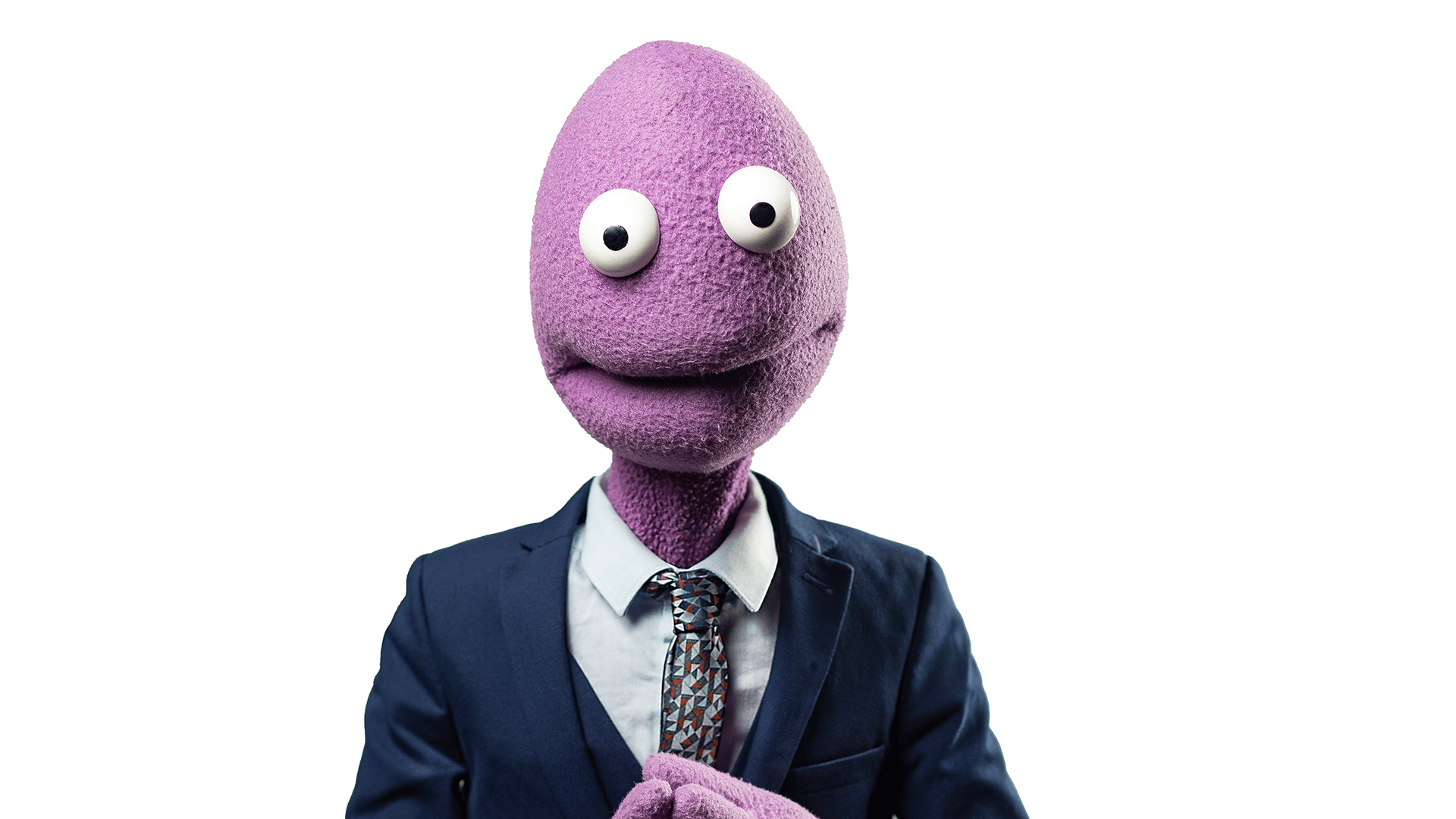 Background: White. Foreground: Randy Feltface, a purple felt puppet wearing a navy suit and white shirt, with their hands clasped together.