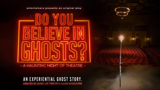 Do You Believe in Ghosts? artwork. Background: (right) A haze-filled theatre auditorium. Rows of red seats lit by a ceiling chandelier. On the stage, a microphone stand holding a bright lightbulb. Foreground: (left) Neon-style red text reads: 'Entertainers presents. DO YOU BELIEVE IN GHOSTS? A HAUNTING NIGHT OF THEATRE. AN EXPERIENTIAL GHOST STORY. Created by James Lee Taylor and Julian Woolford'.