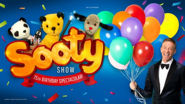 The Sooty Show artwork - Soo (panda bear glove puppet) holding a puppet-sized guitar, Sooty (yellow bear glove puppet) holding a magic wand, and Sweep (grey dog glove puppet) all peeking out from the Sooty logo - yellow letters spelling 'Sooty'. Text reads: The Sooty Show ; 75th anniversary spectacular. A smiling man in a blue, glittery holding a bunch of colourful balloons.
