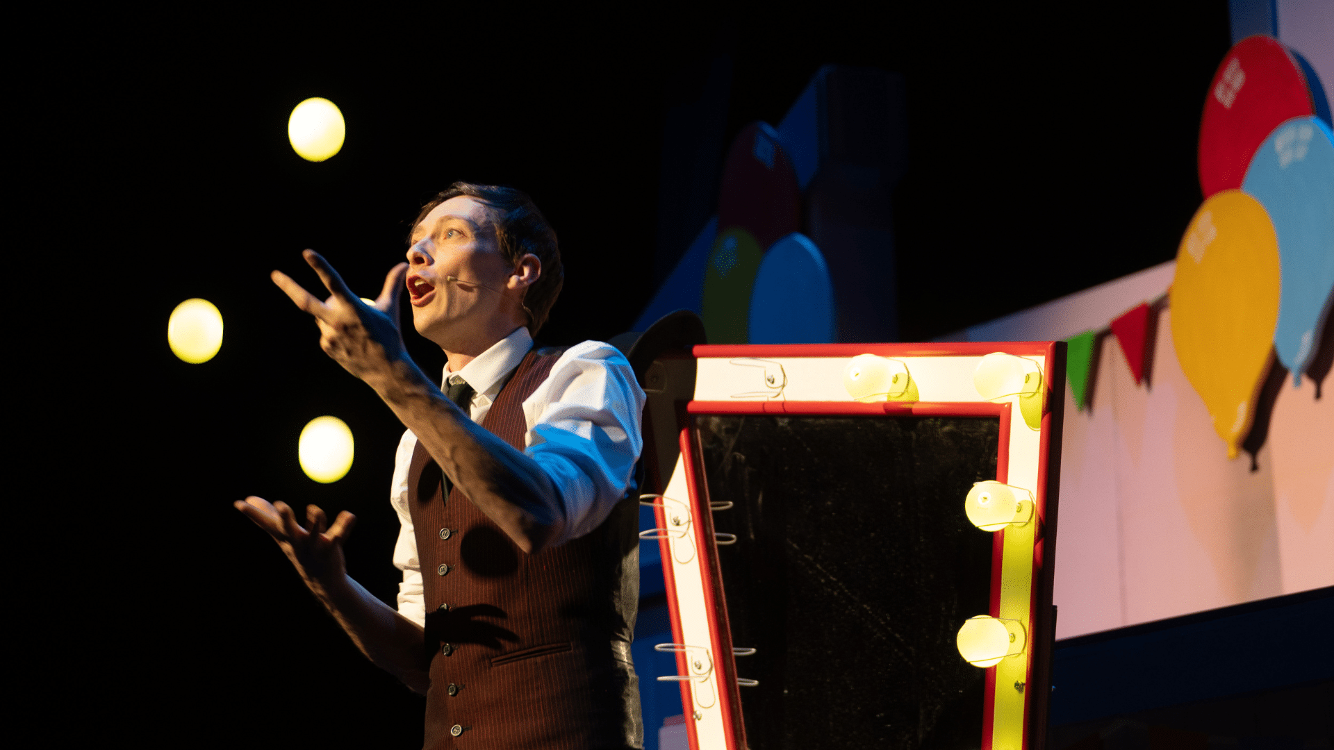 The Sooty Show production image: a man in a brown pinstriped suit stands in front of a dressing-room mirror on stage and gestures towards an off-camera audience.