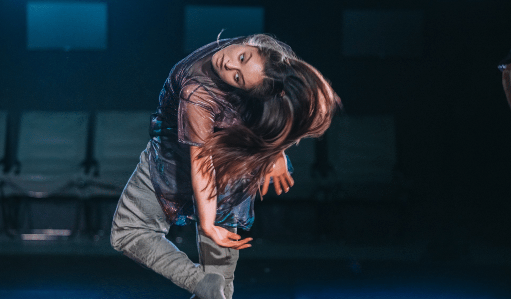 Richard Chappell Dance: Infinite Ways Home production photo - A female dancer in motion, bending backwards, as her long hair swishes.