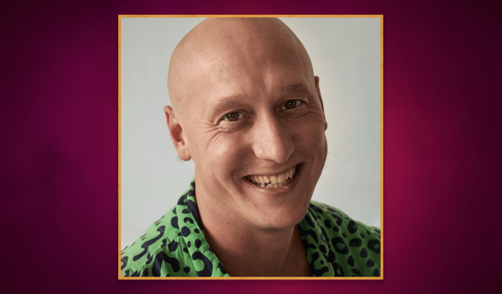 Headshot photo of actor Matt Freeman, a middle-aged white man with no hair, wearing a patterned black and green shirt. The headshot photo has a golden border around it, and is set on top of a purple gradient background.