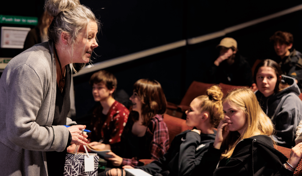 A photograph from Exeter Northcott's Speakers for Schools event: Lisa Hudson stands in the Barnfield Theatre auditorium, smiling at students.