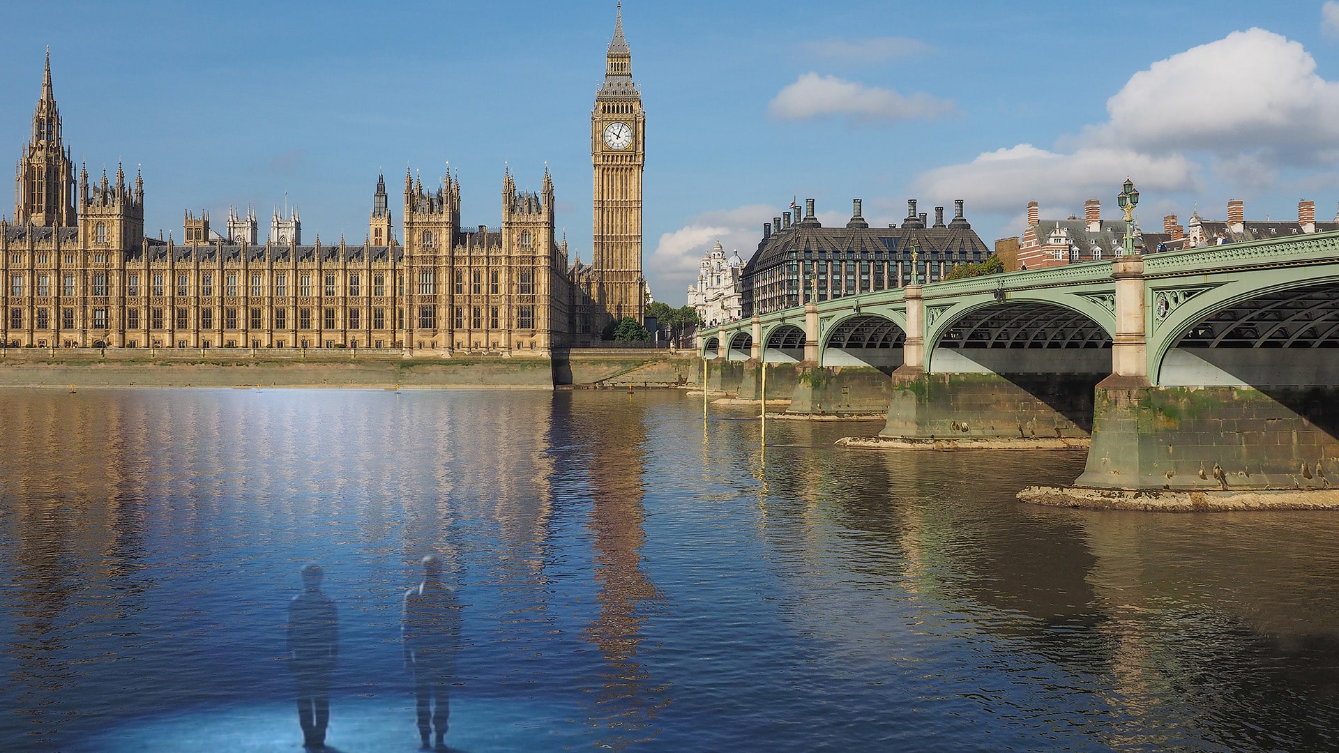 From England with Love artwork. A photograph looking out over The Thames River and Westminster Bridge, a long green metal bridge, in front of the Palace of Westminster, a large light brown stone building, and Big Ben, a large light brown stone clock tower, in London, England. At the bottom left-hand corner of the artwork, two silhouetted figures stand in the river water.