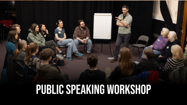 A photo of Martin Berry, Exeter Northcott's Creative Director, leading a workshop. He stands in front of a blank flip chart in the centre of a circle of seated attendees of diverse ages listening with rapt attention. Text reads 'Public Speaking Workshop'