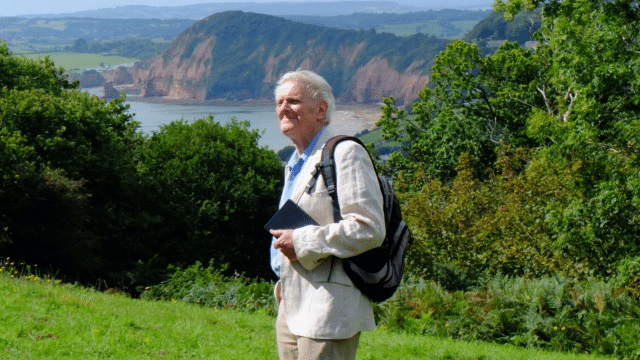 A photo of Paul Jesson in hiking clothing, standing in a coastal Devon landscape.