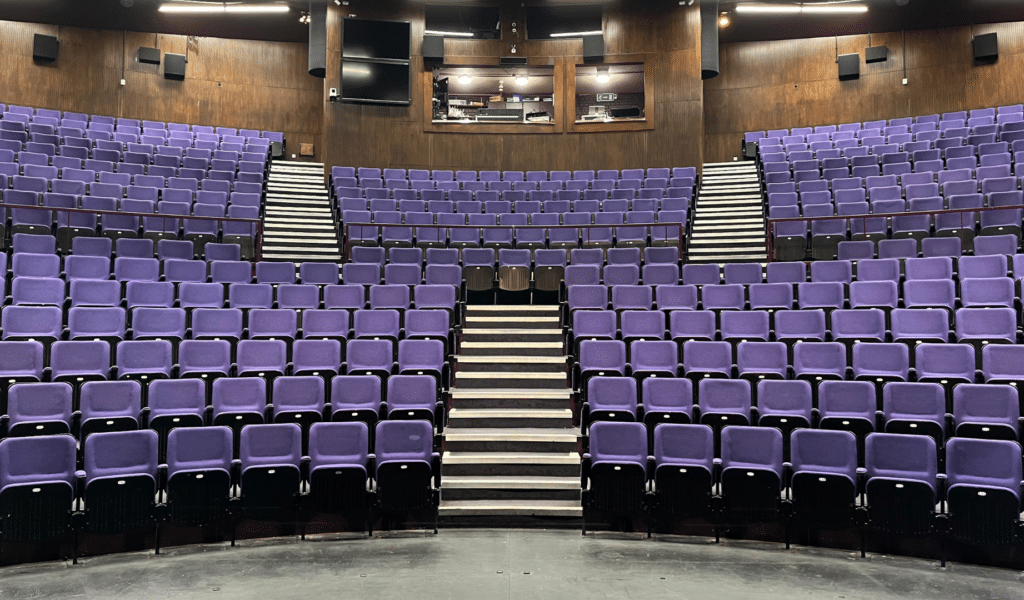 A photo taken from the stage of Exeter Northcott Theatre, looking out at two tiers of seating upholstered in purple.