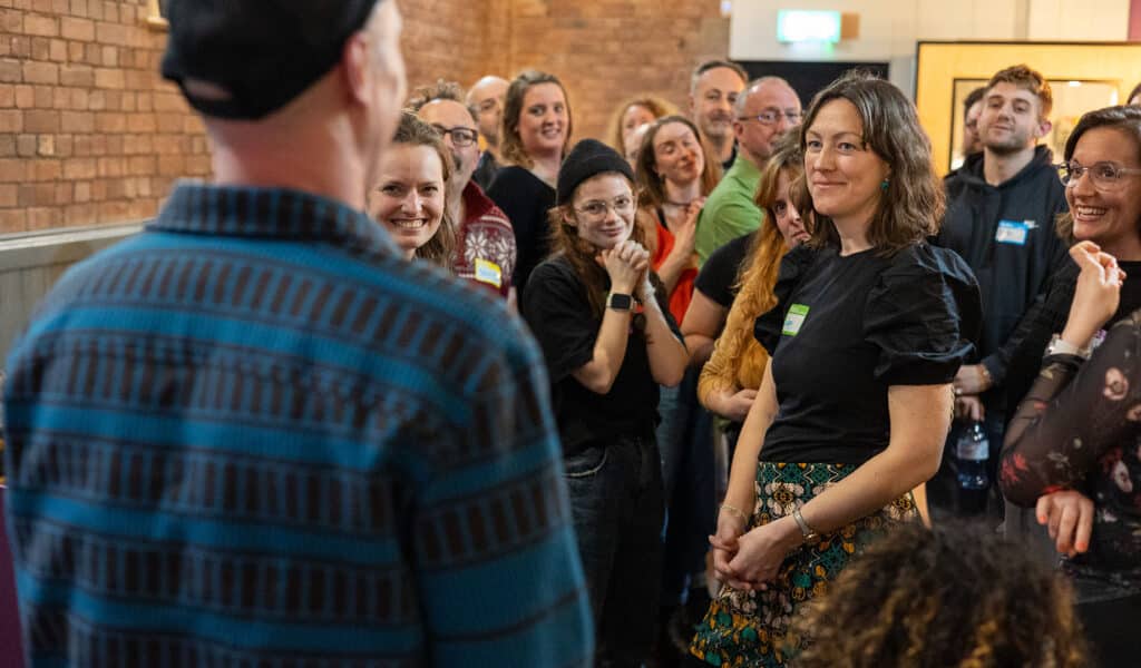 A group of Fail Space participants stand and listen intently to another participant in the Barnfield Theatre's bar.