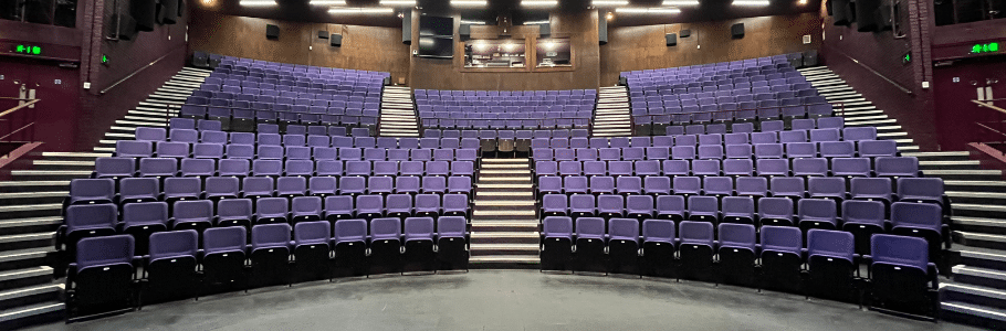 A photo taken from the stage of Exeter Northcott Theatre, looking out at two tiers of seating upholstered in purple.
