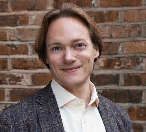 Headshot of Tom Littler against a brick wall.