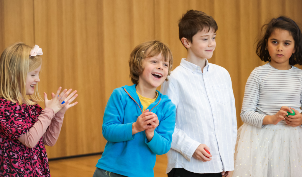 Photo of four children stood side-by-side in a wood-panelled studio, laughing and clapping.