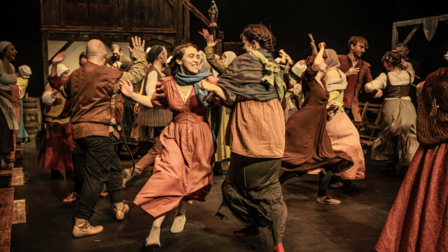 Photo of The Commotion Time cast, dressed in Tudor clothing, dancing joyfully.