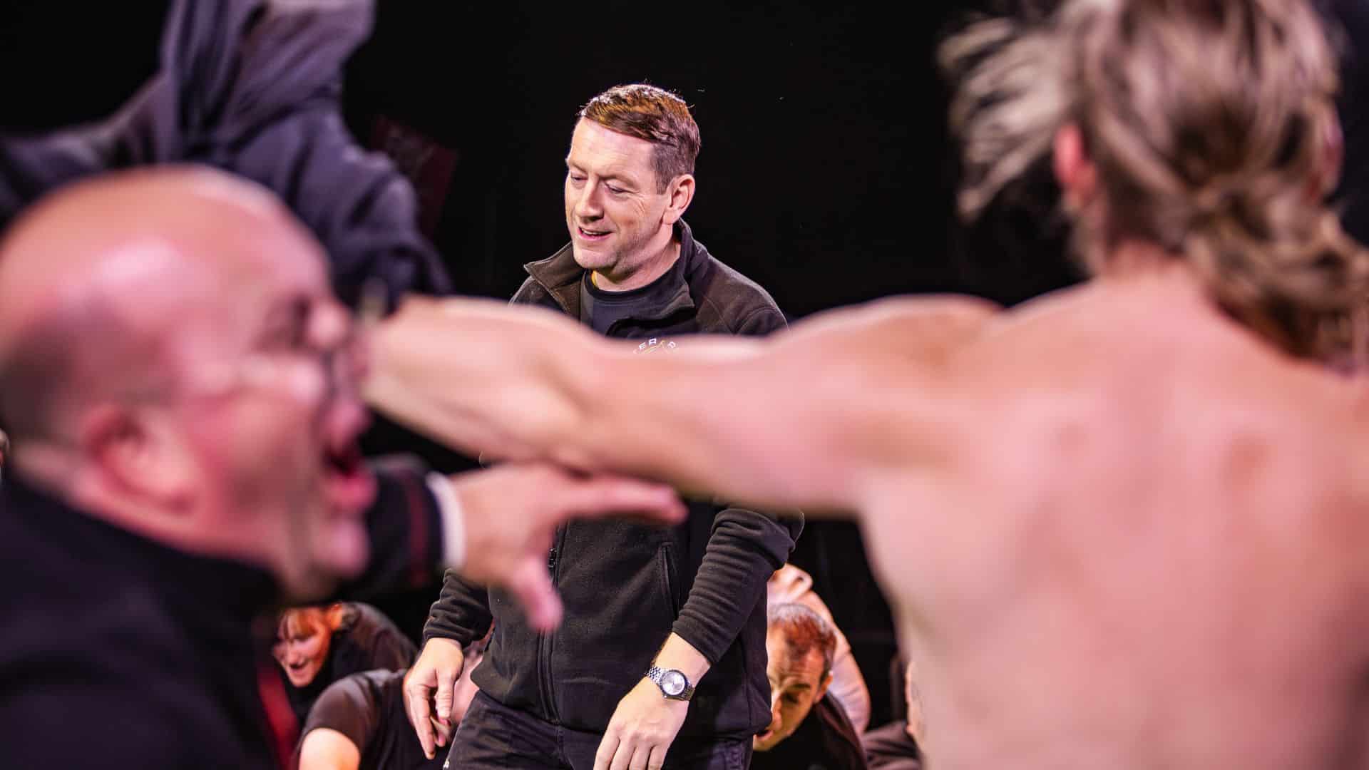 Rugby players celebrating. One has his back to the camera, swinging his shirt around. Central is the Rob Baxter (coach) character).
