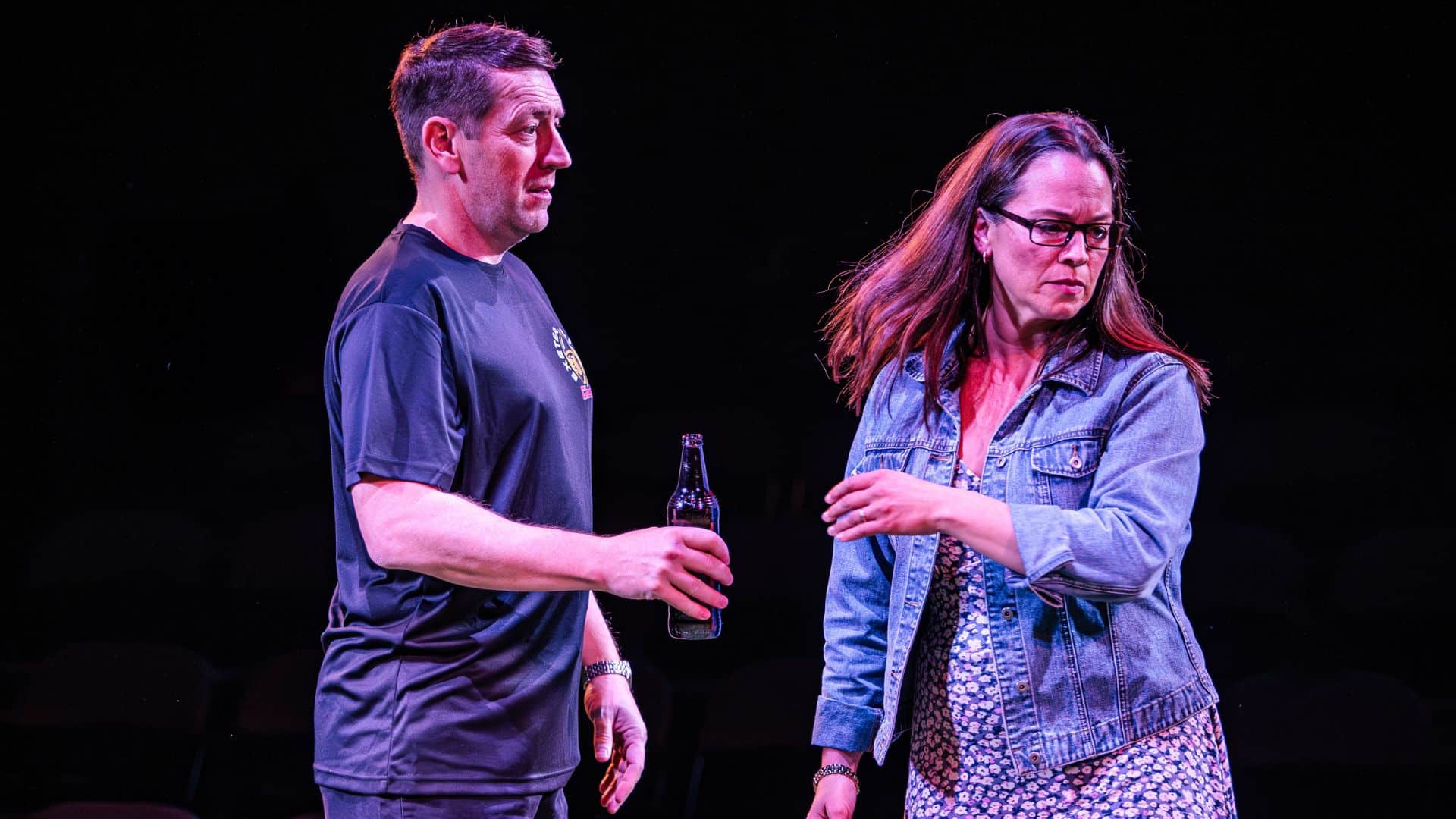 Actors portraying Rob Baxter and Jo Baxter. He is holding a beer, looking at her and she is turning away from him.
