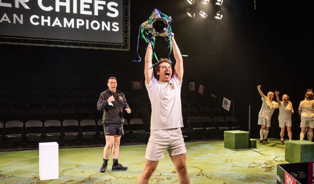 Exeter Chiefs player is holding the winning Cup above his head, cheering.