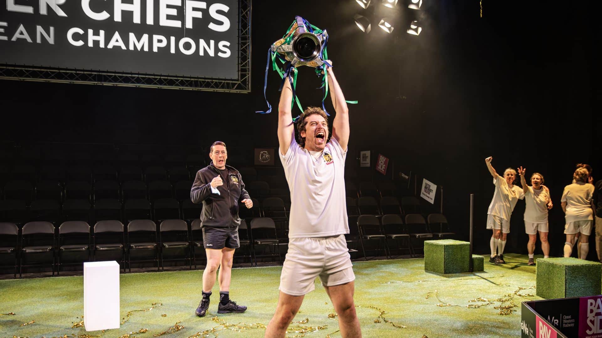Exeter Chiefs player is holding the winning Cup above his head, cheering.
