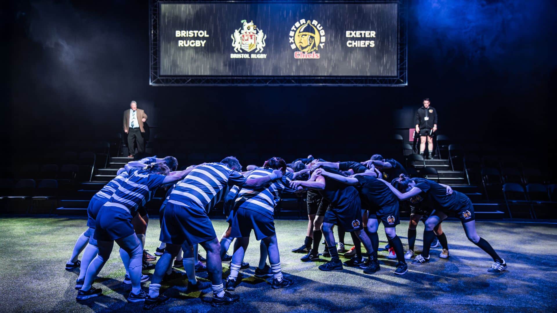 Exe Men production image. The Northcott stage has been transformed into Sandy Park rugby stadium. Players are in a scrum.