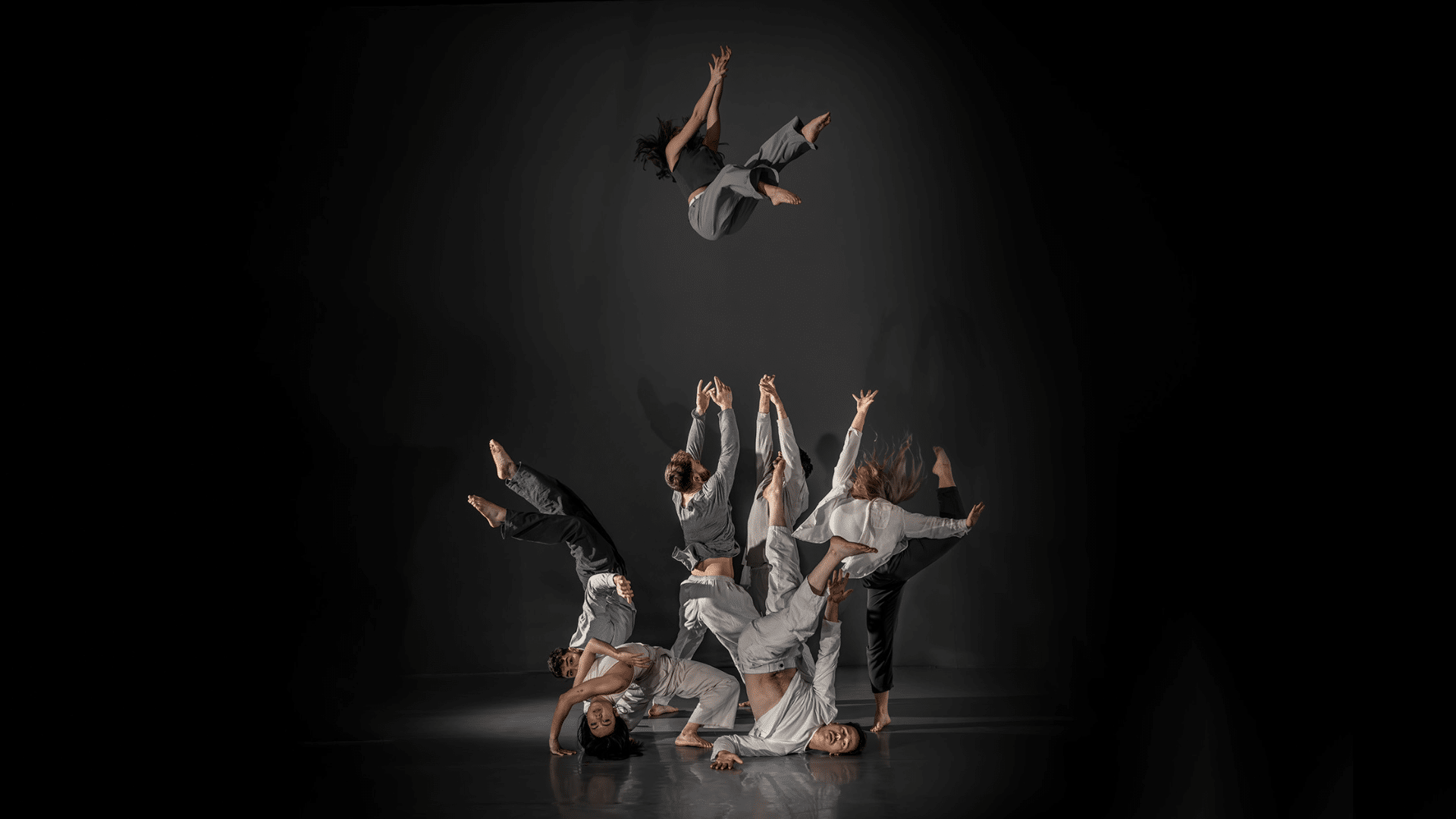Hidden promotional artwork: dancers in grey and black tops and trousers gather in the middle of the stage, all in different poses. Two dancers in the middle throw another dancer high into the air above them.