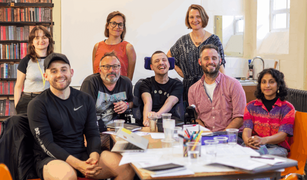 Photo of a group of artists gathered around a table and smiling at the camera.
