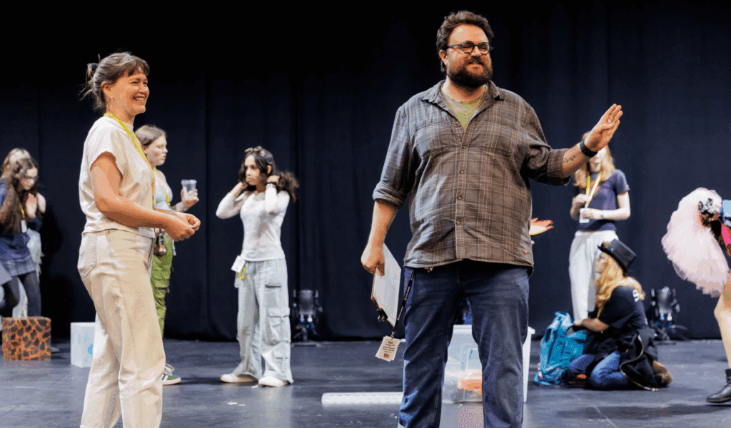 Photo of a youth theatre leader on the Northcott stage, surrounded by young people.