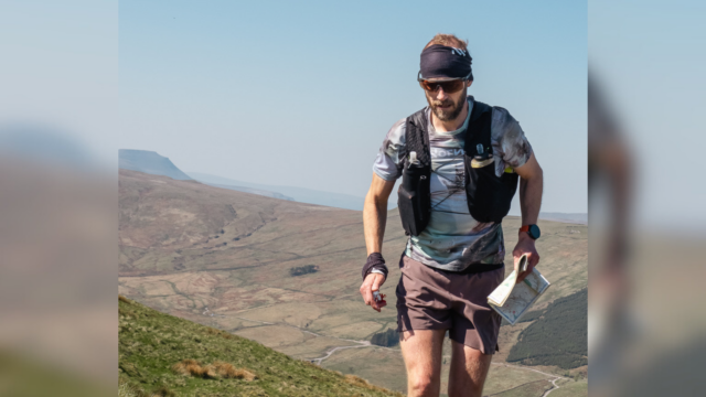 A photograph of Damian Hall wearing running kit whilst walking through a vast landscape.
