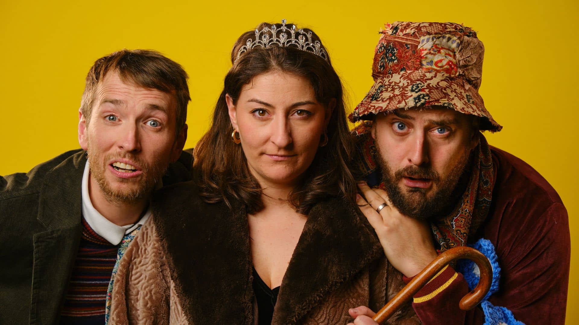 Andrew Armfield, Jodie Micciché and Peter Watts pose in character against a yellow background.