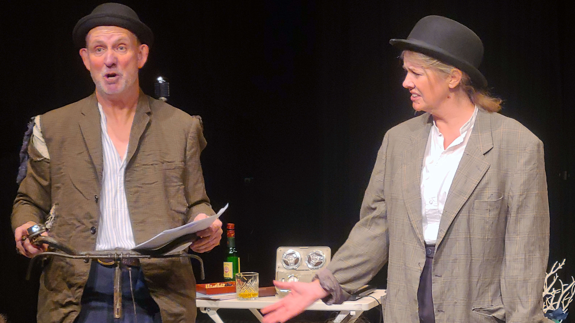 A photograph of two performers on stage wearing shabby suit jackets and bowler hats.