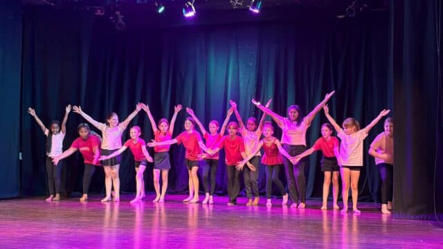 A group of children on stage, spreading their arms into the air.