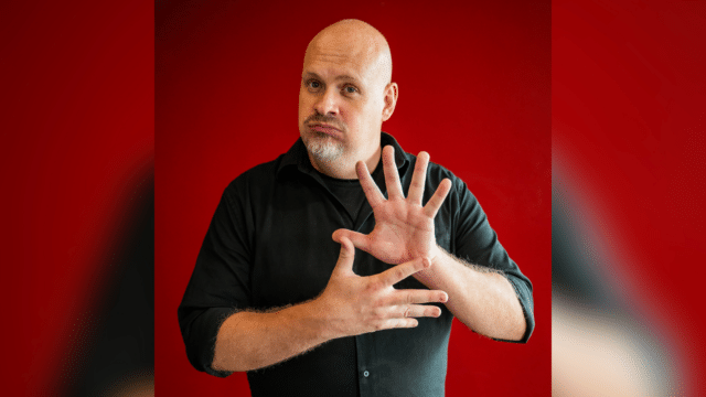 A photograph of Gavin Lilley against a red background using BSL.