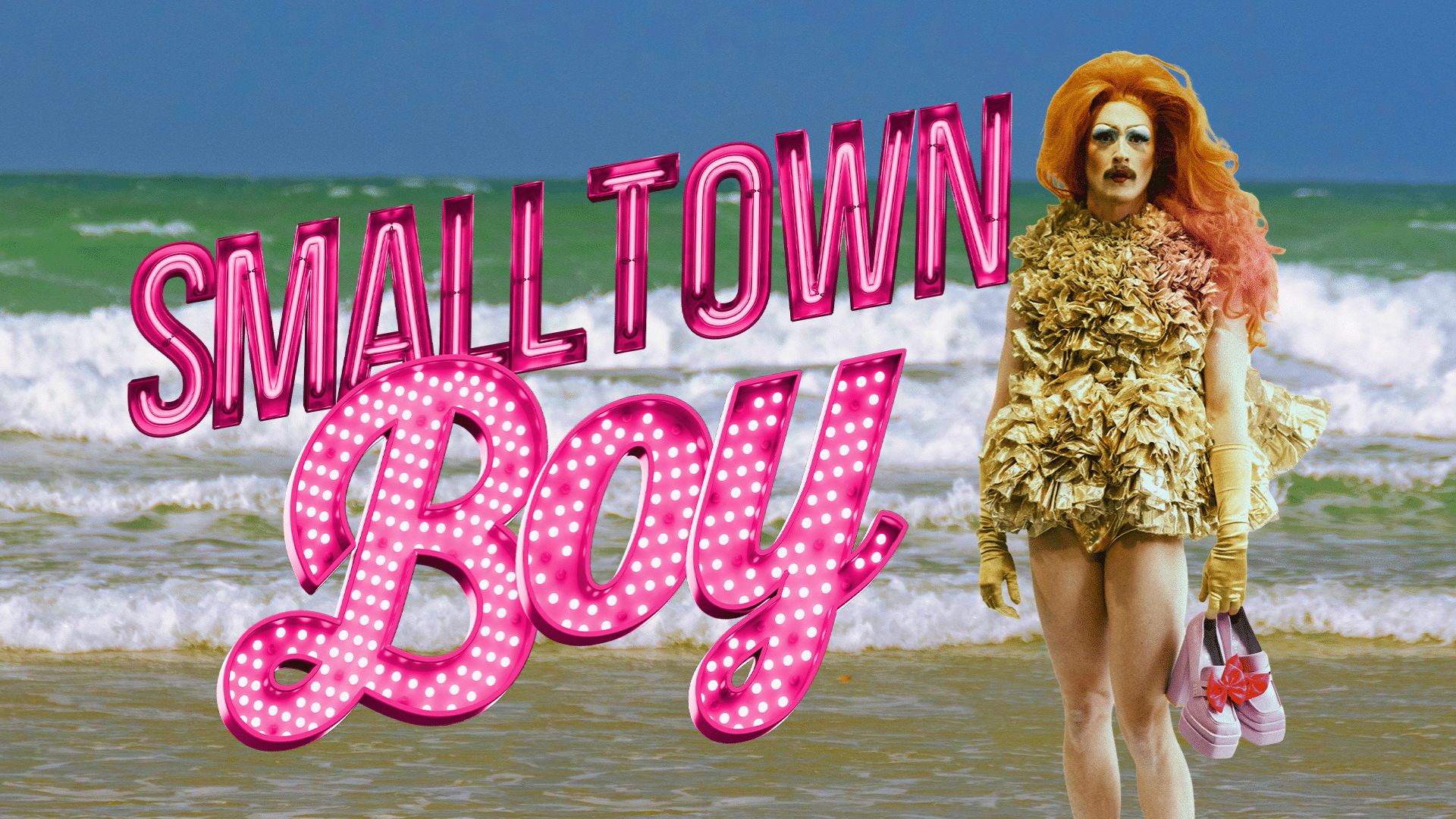 A photograph of a drag queen with a moustache standing on a beach. They are wearing a short gold dress and holding a pair of pink heels. Text in large neon pink font reads: 'Smalltown Boy'.