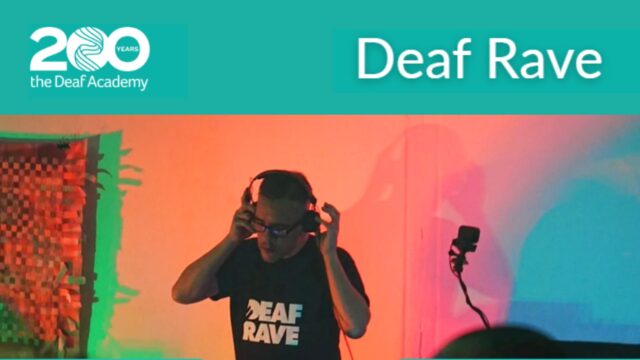 An image of a DJ with luminescent lights in t he backdrop. He is holding his headphones and his t-shirt says