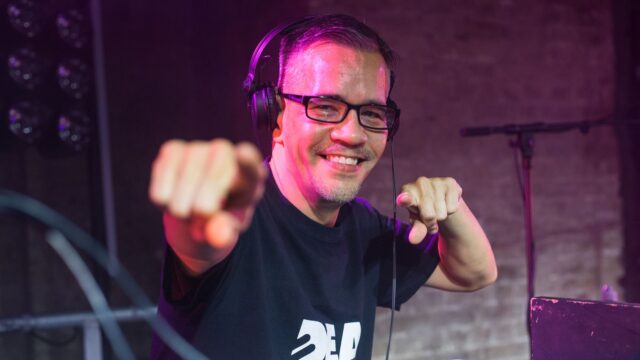 A photo of Troi Lee MBE, Deaf Rave organiser, pointing to the camera and smiling.
